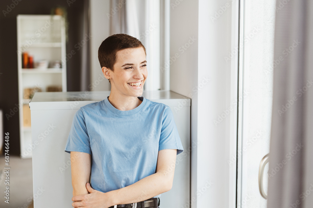 Laughing Young Woman in Blue T-Shirt, Short Hair, Glancing Happily in Modern Living Room Laughing Young Woman in Blue T-Shirt, Short Hair, Glancing Happily in Modern Living Room