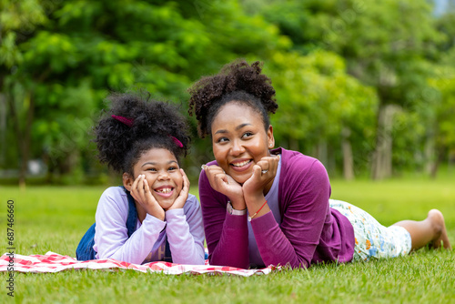 African American mother and young daughter are lying down after having a summer picnic in the public park for weekend leisure and happiness