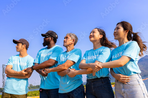 Team of young and diversity volunteer workers group enjoy charitable social work outdoor in the beach cleaning project wearing blue t-shirt while joining hand in assemble unity photo