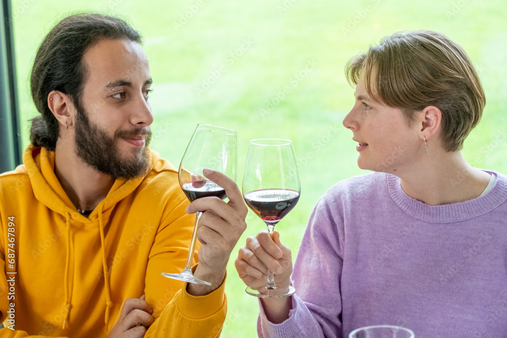 This image captures a candid moment between two friends sharing a toast with glasses of red wine. Engaged in friendly conversation, they are dressed in casual, cozy sweaters, symbolizing comfort and This image captures a candid moment between two friends sharing a toast with glasses of red wine. Engaged in friendly conversation, they are dressed in casual, cozy sweaters, symbolizing comfort and
