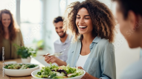 Young woman is laughing with her friends at party as she holding bowl a salad on white kitchen.