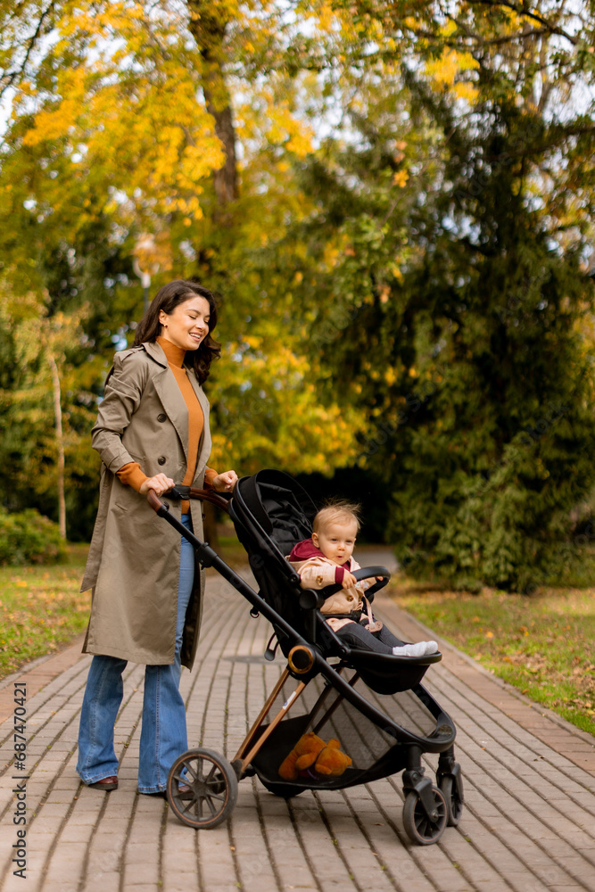 Young woman with cute baby girl in baby stroller at the autumn park Young woman with cute baby girl in baby stroller at the autumn park