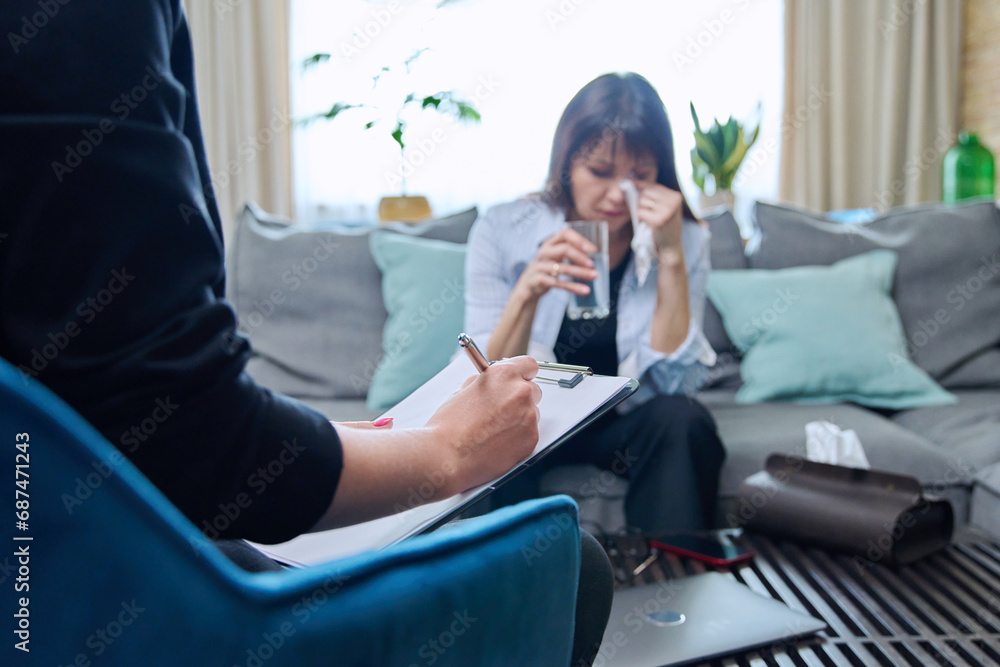 Sad crying middle-aged woman sitting on couch in therapy with psychologist