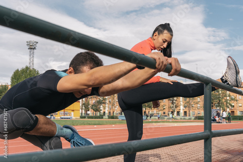 Couple of athletes stretching their back muscles against a railing. Side image of a young couple finishing their training by performing exercises to relax the upper body muscles.