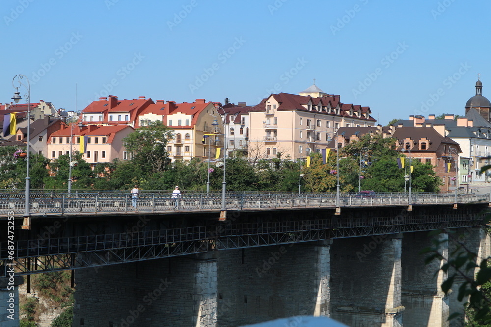 A bridge on high pillars leads into the city. Low-rise buildings in the city.