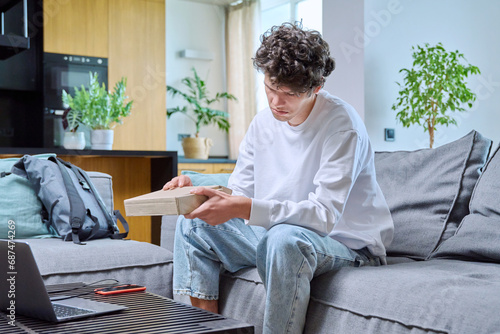 Young male unpacking an online purchase, sitting on couch at home