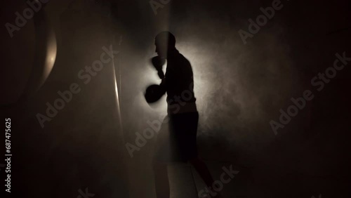 Male boxer impacting on punching bag over black smoke background. Boxer training hard. photo