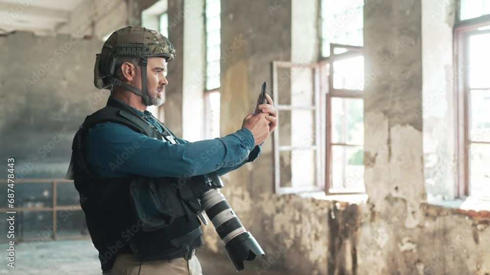 Close view of Caucasian male with grey beard using his mobile device to look for news or work related information. Working at military conflict location. Press worker hiding in abandoned building. Close view of Caucasian male with grey beard using his mobile device to look for news or work related information. Working at military conflict location. Press worker hiding in abandoned building.