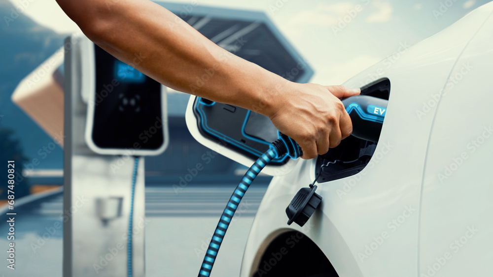 Asian man insert EV charger and recharge his electric car recharging energy from future home charging station. Smart and futuristic home energy infrastructure. Peruse