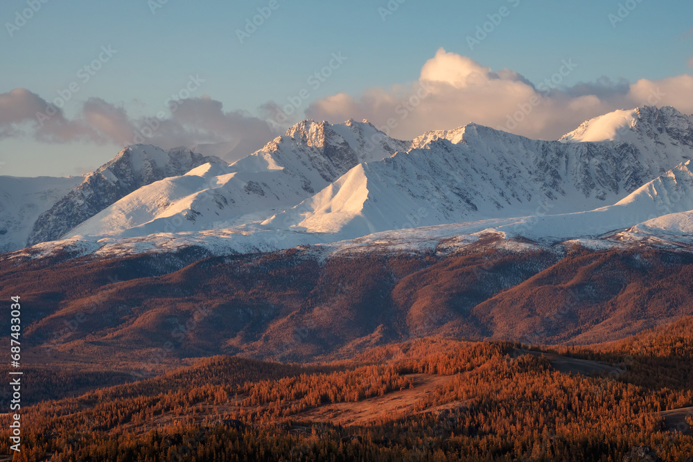 Autumn snow mountains at sunset. Bright panoramic mountain landscape with a snowy rock in golden sunlight. Natural background of a walk through the rocky mountains with sharp rocks and blue sky.