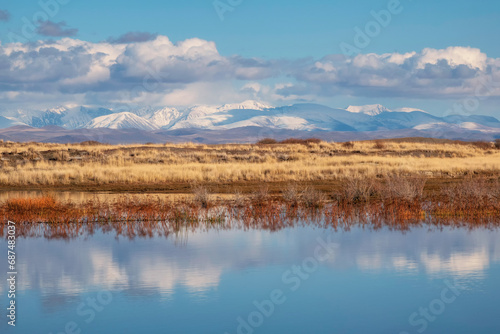 Beautiful autumn mountain lake and mountains. Reflection of snowy peaks and dry yellow grass in the steppe on the surface of a mountain lake.