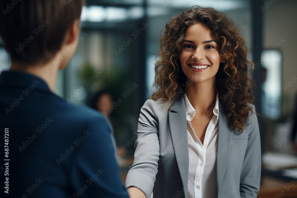 Bellissima donna manager sorridente con capelli lunghi in un moderno ufficio con abito elegante mentre stringe la mano ad un cliente