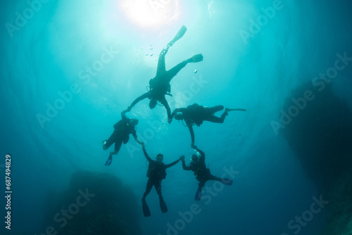 Silhouettes of a group of scuba divers forming a circle holding hands around the sun underwater