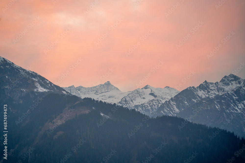 red orange dusk dawn colors over snow covered himalaya mountains and fluffy clouds showing hill stations in jhibbi kullu manali