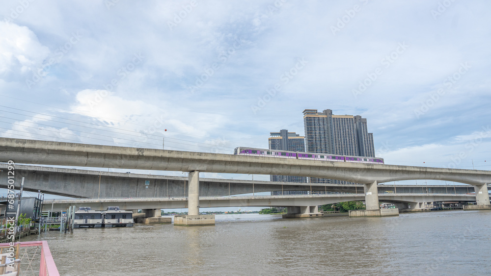 Image of a train driving through a river. On a large concrete bridge There is a large bridge over the river next to it. One more place too.