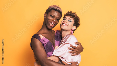 Stylish trans men in make up and fashion clothes embracing and smiling on yellow photo