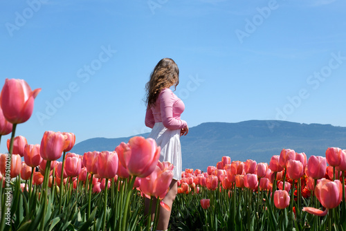 Young girl tourist in pink dress and straw hat standing in blooming tulip field. Spring time photo