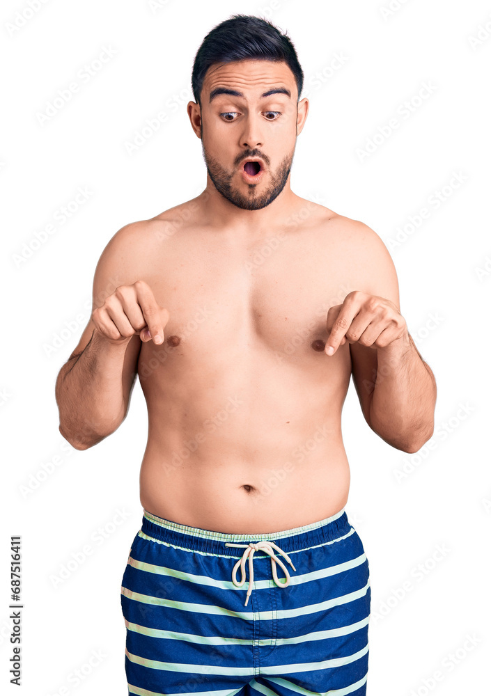 Fototapeta premium Young handsome man wearing swimwear pointing down with fingers showing advertisement, surprised face and open mouth
