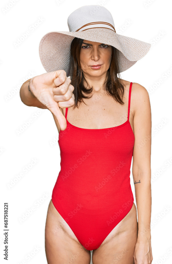Beautiful brunette woman wearing swimsuit and summer hat looking unhappy and angry showing rejection and negative with thumbs down gesture. bad expression. Beautiful brunette woman wearing swimsuit and summer hat looking unhappy and angry showing rejection and negative with thumbs down gesture. bad expression.