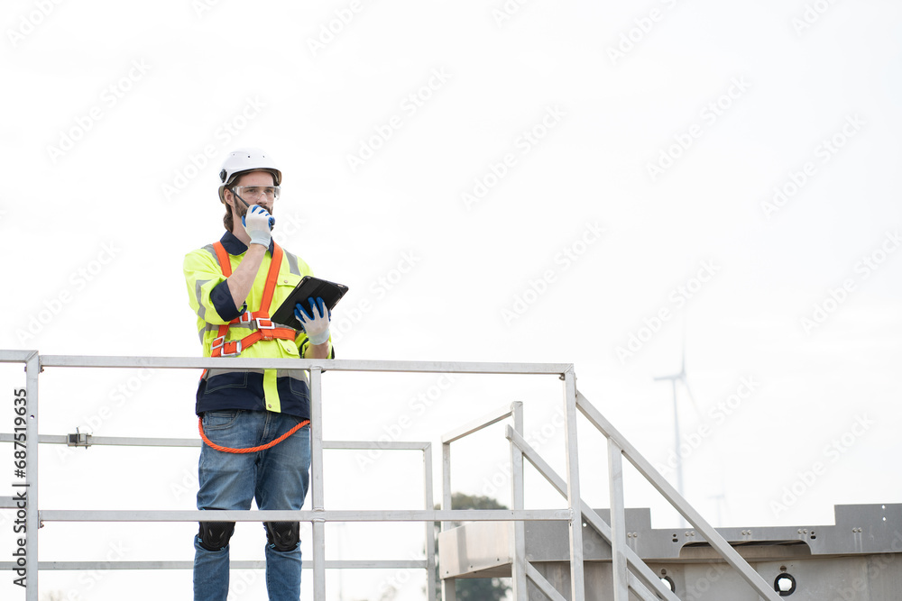 Male engineer using radio communication at windmill field farm. Male engineer working at at wind turbines farm Male engineer using radio communication at windmill field farm. Male engineer working at at wind turbines farm