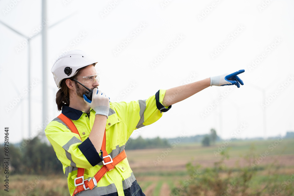 Male engineer using radio communication at windmill field farm. Male engineer working at at wind turbines farm Male engineer using radio communication at windmill field farm. Male engineer working at at wind turbines farm