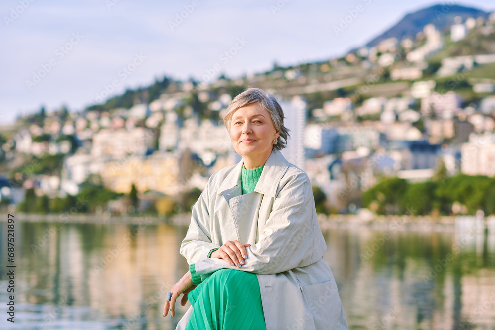 Outdoor portrait of happy mature 50 - 55 year old woman, enjoying nice spring day by the lakeside, wearing grey coat - obrazy, fototapety, plakaty 