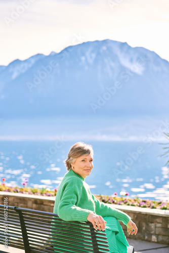 Portrait of middle age woman enjoying nice day outside, relaxing on bench in front of mountain lake