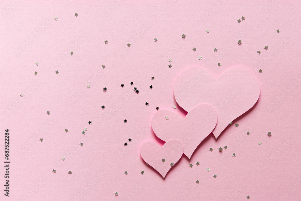 Delicate pink background, three pink hearts cut out of paper and confetti stars. Greeting card. Flat lay, top view, copy space. Design for Valentine's Day February 14th.