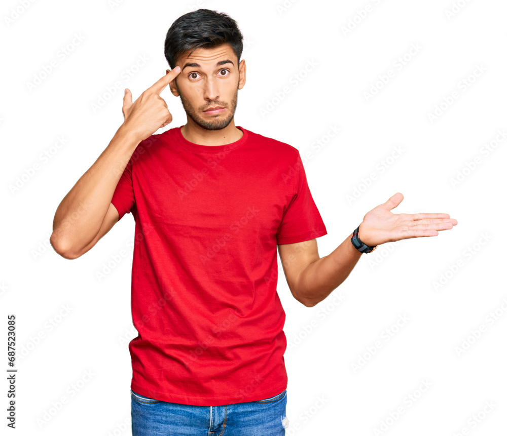 Young handsome man wearing casual red tshirt confused and annoyed with open palm showing copy space and pointing finger to forehead. think about it. Young handsome man wearing casual red tshirt confused and annoyed with open palm showing copy space and pointing finger to forehead. think about it.