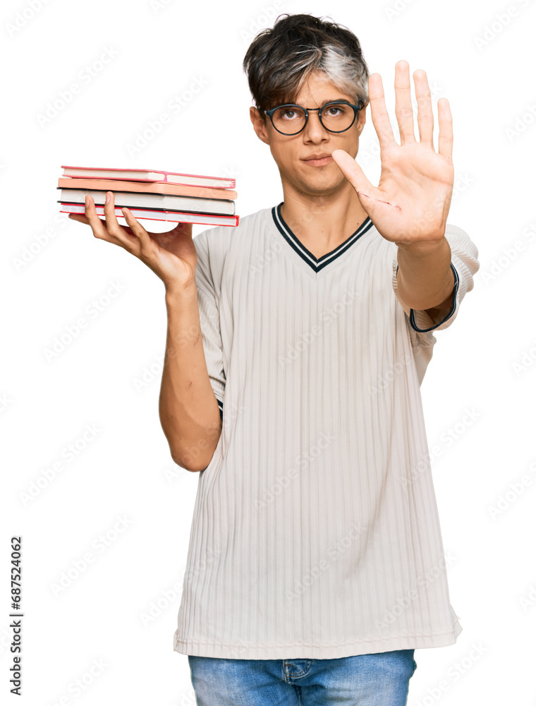 Young hispanic man holding books with open hand doing stop sign with serious and confident expression, defense gesture Young hispanic man holding books with open hand doing stop sign with serious and confident expression, defense gesture