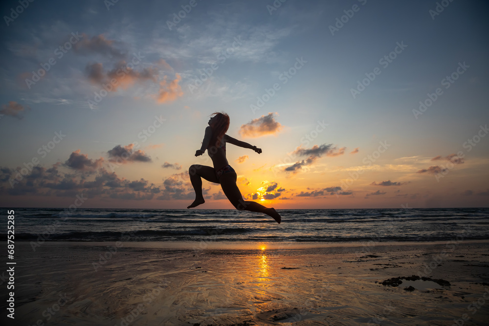 A beautiful girl in a swimsuit jumps at sunset. Sunny colorful sunset. Seashore on the beach.