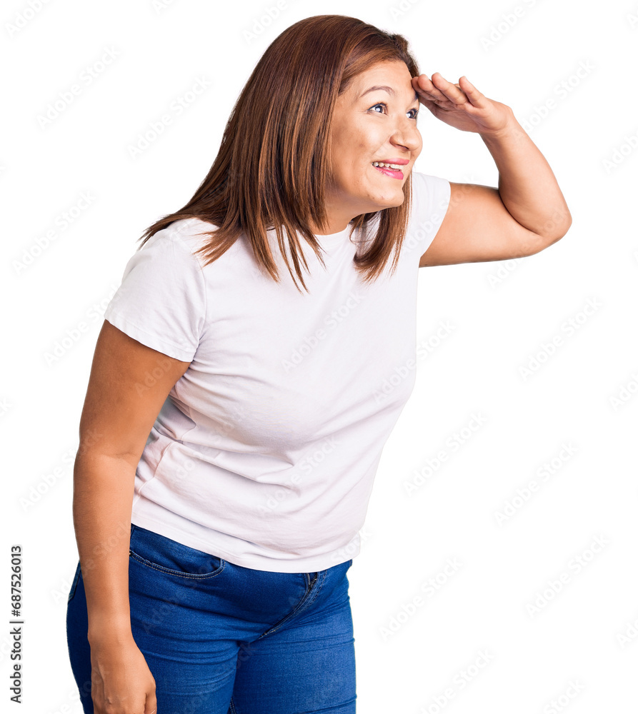 Middle age latin woman wearing casual white tshirt very happy and smiling looking far away with hand over head. searching concept. Middle age latin woman wearing casual white tshirt very happy and smiling looking far away with hand over head. searching concept.