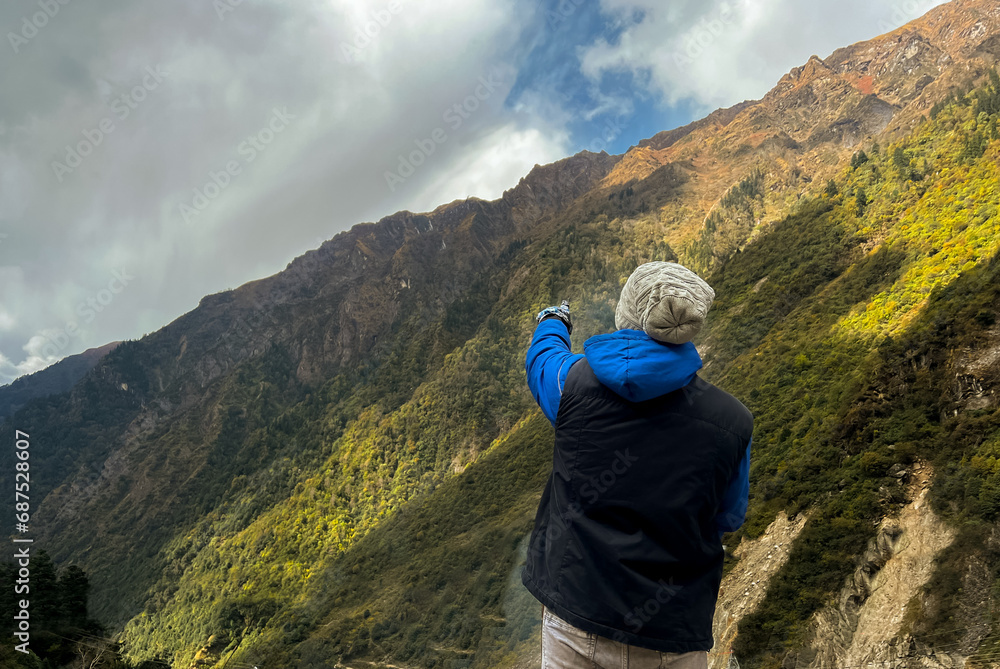 Portrait of a hiker standing in a cliff and pointing hands towards mountains wearing sweater and gloves. Selective focus on subject with the copy space for inscription. Rear view, scenary,  landscape 