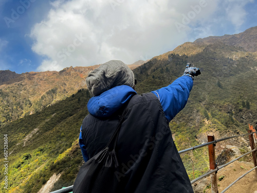 Portrait of a hiker standing in a cliff and pointing hands towards mountains wearing sweater and gloves. Selective focus on subject with the copy space for inscription. Rear view, scenary,  landscape 