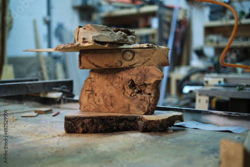 A captivating sculpture of wood burls piled atop one another awaits the creative touch of a woodworker in the midst of a sawdust-filled workshop.