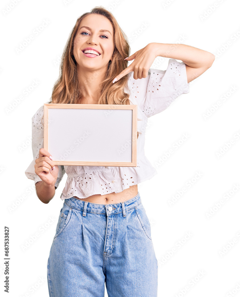 Young caucasian woman with blond hair holding blank empty banner pointing finger to one self smiling happy and proud Young caucasian woman with blond hair holding blank empty banner pointing finger to one self smiling happy and proud