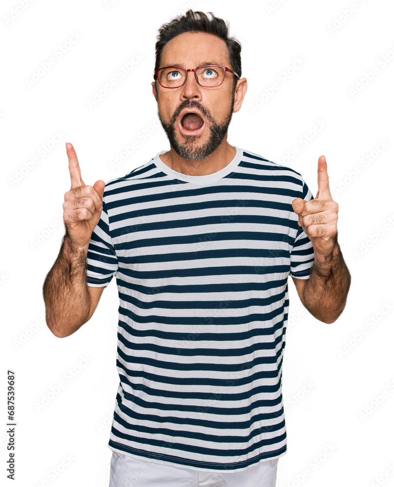 Middle age man wearing casual clothes and glasses amazed and surprised looking up and pointing with fingers and raised arms. Middle age man wearing casual clothes and glasses amazed and surprised looking up and pointing with fingers and raised arms.