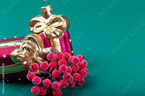 Beautiful red Christmas tree decorations in form of gifts and frozen bright rowan berries on green background with copy space close-up. Happy Holidays