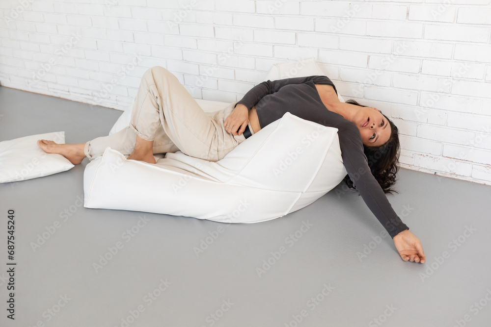 An attractive brunette woman is resting lying on the sofa, joking, pretending to be tired and tomfoolery, dressed in casual clothes, light pants and a long-sleeve sweater An attractive brunette woman is resting lying on the sofa, joking, pretending to be tired and tomfoolery, dressed in casual clothes, light pants and a long-sleeve sweater