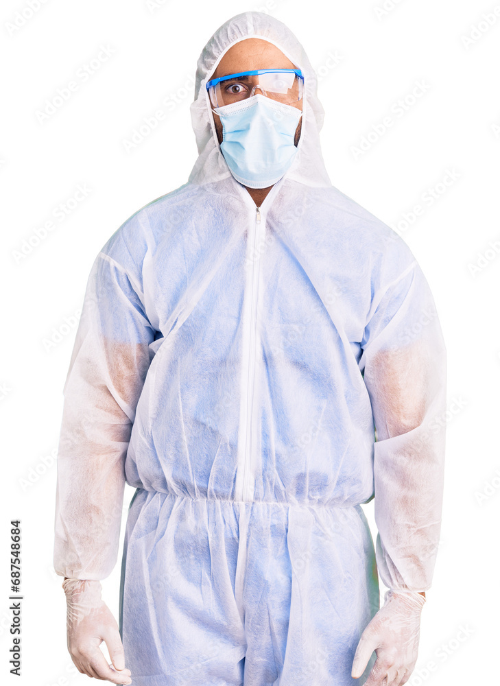 Young hispanic man wearing doctor protection coronavirus uniform and medical mask afraid and shocked with surprise expression, fear and excited face. Young hispanic man wearing doctor protection coronavirus uniform and medical mask afraid and shocked with surprise expression, fear and excited face.