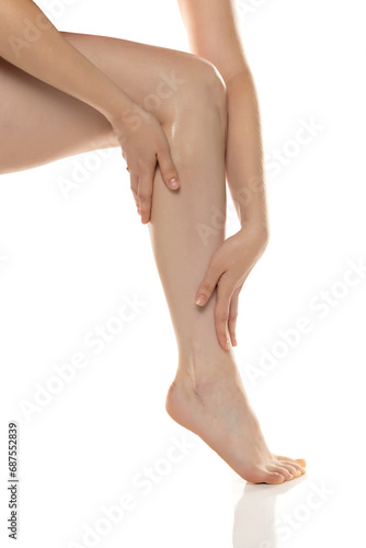 Young woman  applies cosmetic product on her legs on white background. © vladimirfloyd