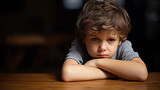 Boy with arms crossed leaning on the table, head resting on his arms. Child with sad worried face.