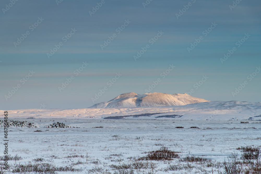 View over the snow-covered flat volcanic landscape in Iceland with snowy mountains in skimming morning sunlight in background against a clear blue sky