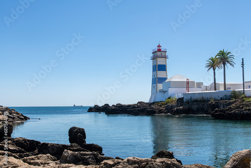 View over water of Cascais Bay in front of Santa Marta Lighthouse with white tiles, blue horizontal stripes and a red lantern in Cascais, Lisbon District, Portugal on the estuary of the River Tagus photo