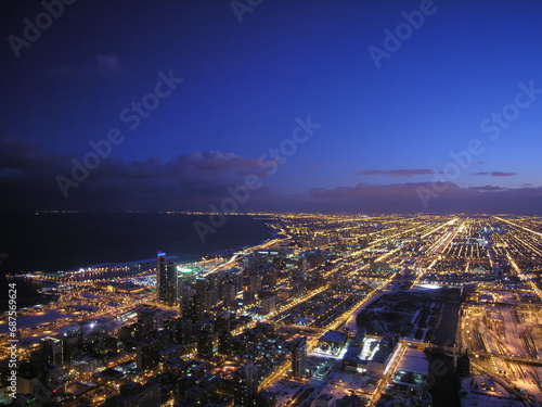 A panoramic aerial view of the urban landscape of Chicago and Lake Michigan at night with vibrant lights, modern architecture, and clouds.