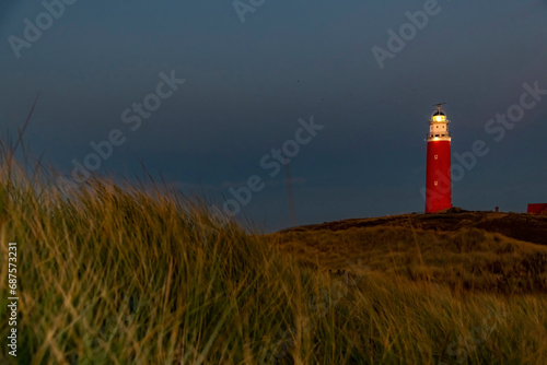 Panoramic view of the historical red lighthouse at the north end of the island of Texel  The Netherlands in the dark of the evening with some dune grass or marram grass in the forefront