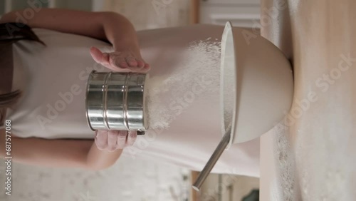Woman is sifting flour through a metal sifter, hand closeup view. Preparing flour for baking cake in kitchen at home. Prepares dough for baking pizza bread, process of sifting flour in the bakery shop