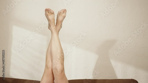 Relaxed woman moving legs upside down while resting on couch. Female feet barefoot on background of light wall with copy space. photo