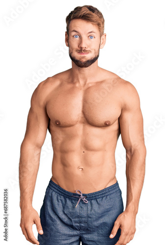 Young caucasian man standing shirtless puffing cheeks with funny face. mouth inflated with air, crazy expression. photo