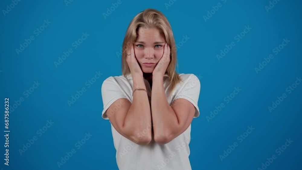 Shocked young woman is grabbing her head looking mad and upset standing isolated over a blue background in the studio Shocked young woman is grabbing her head looking mad and upset standing isolated over a blue background in the studio